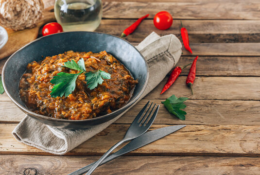 Traditional Georgian dish Ostri in a black bowl with meat pieces, vegetables, and herbs, surrounded by ingredients on rustic wooden table. Selective focus