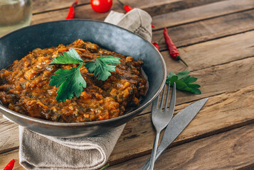Traditional Georgian dish Ostri in a black bowl with meat pieces, vegetables, and herbs, surrounded by ingredients on rustic wooden table. Selective focus