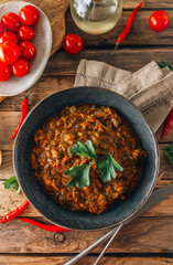 Traditional Georgian dish Ostri in a black bowl with meat pieces, vegetables, and herbs, surrounded by ingredients on rustic wooden table. Top view