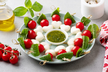 Mozzarella cheese, cherry tomatoes and basil skewers, romantic appetizers on a plate. Grey background. Close up.