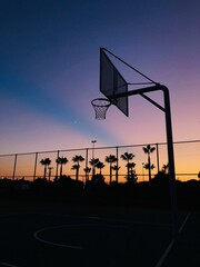 basketball court, sunset sky, urban landscape, outdoor sports, silhouette photography, palm trees, fenced basketball hoop, serenity, golden hour, poster design, minimalist sunset, athletic vibes © Yaln