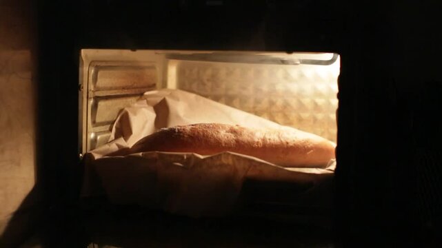 A baguette of white bread is baked in an electric oven, and the hand takes out the finished product.