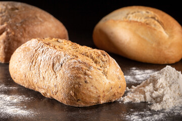 A loaf of fresh bread and a pile of flour on a black background