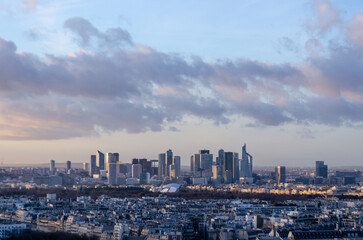 A panoramic view of La Défense business district in Paris, France. The modern skyscrapers and the city skyline are visible against a cloudy sky during a sunset