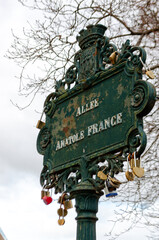 Vintage "Allée Anatole France" street sign in Paris, France, decorated with love locks. Urban detail with history and romance during a cloudy day.