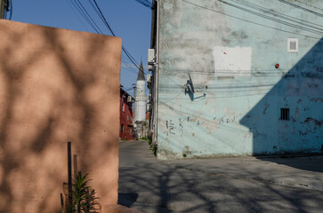 Narrow street or alleyway in an urban setting with a mosque minaret in the background. Colorful walls and urban details.