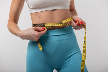 Beautiful slim healthy woman fitness lady measuring waist with yellow measuring tape on grey background