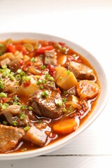 Delicious stew with vegetables in bowl on white wooden table, closeup