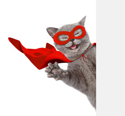 Happy cat wearing superhero costume looking above from behind blank white banner and waves his paw. Isolated on white background. © Ermolaev Alexandr