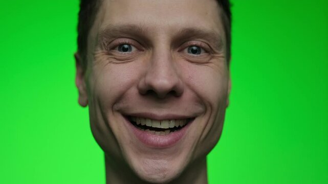 A young man smiles warmly, his laugh lines visible, expressing genuine happiness. Portrait of a cheerful male on a green chroma key background.