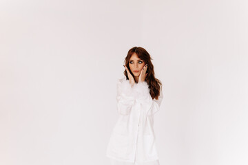 A sad woman worries and holds her hands to her face and head while standing on a white isolated background. Space for the text. A place for advertising and marketing. Copy space