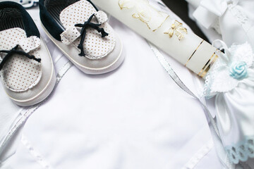 Baptism Ceremony Preparations. Candle, baby shoes, and white robe fabric for a holy event. Elegant details for children's fashion and accessories. Empty copy space christening background.