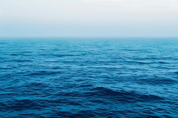 Obraz premium A serene image of a calm ocean under a misty sky. The deep blue water shows gentle waves, creating a peaceful and tranquil maritime scene. The horizon is barely visible in the light mist.