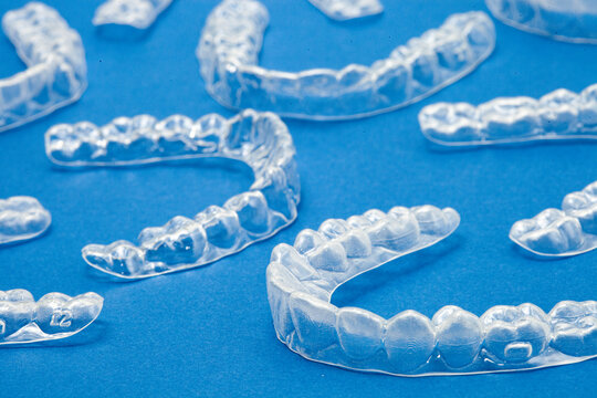 Transparent invisible dental aligners or braces aplicable for an orthodontic dental treatment. Many transparent aligners lie in a row on a black background. Transparent invisible dental ali