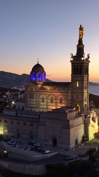 vertical view: aerial shot of Marseille cathedral at night illuminated, drone view of Notre Dame de la Garde in France, travel in French Riviera