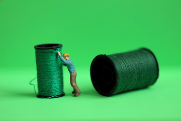 miniature worker with  green thread reel on green background.