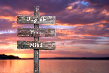 upgrade your mind text quote on wooden signpost outdoors by the lake during red dramatic sunset.
