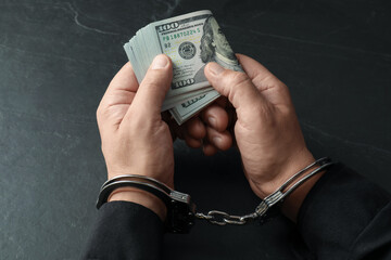 Corruption. Man in handcuffs holding dollar banknotes at grey textured table, closeup