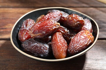 Many tasty dried dates in bowl on wooden table, closeup