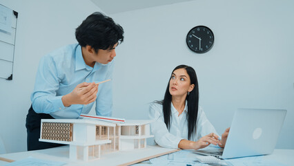 Professional male asian architect using ruler to measure house model length while young beautiful...