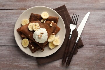 Delicious chocolate crepes with banana, nuts and scoop of ice cream on wooden table, flat lay