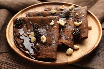 Delicious chocolate crepes with pine cone jam and nuts on wooden table, closeup