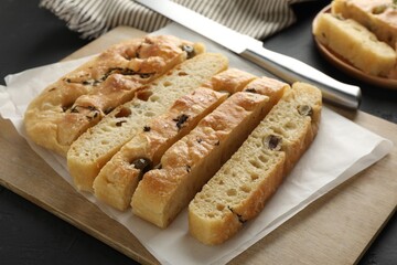 Slices of delicious focaccia bread with olives, thyme, salt and knife on black table, closeup