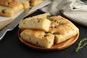 Slices of delicious focaccia bread with olives, thyme and salt on black table, closeup