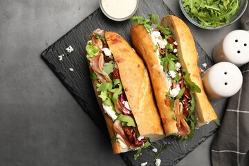 Halves of baguette sandwich with prosciutto and sun dried tomatoes and ingredients on grey table,...