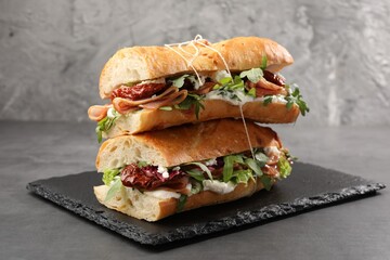 Halves of baguette sandwich with prosciutto and sun dried tomatoes on grey table