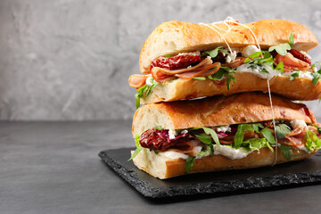 Halves of baguette sandwich with prosciutto and sun dried tomatoes on grey table, closeup. Space for text