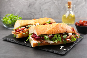 Halves of baguette sandwich with prosciutto and sun dried tomatoes on grey table, closeup