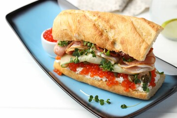 Delicious baguette sandwich with caviar, ham and capers on white wooden table, closeup
