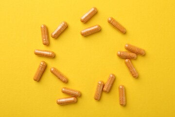 Turmeric capsules on yellow background, flat lay. Space for text