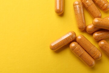 Many turmeric capsules on yellow background, flat lay. Space for text