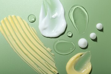 Cream and gel samples on green background, top view