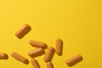 Many turmeric capsules on yellow background, flat lay. Space for text