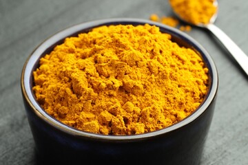 Turmeric powder in bowl on grey table, closeup