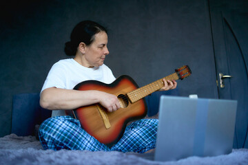 Obraz premium a senior woman learns to play the guitar with online lessons