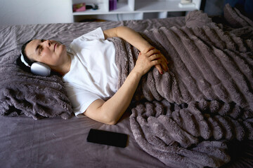 a senior woman wearing sonic hues sleep headphones sleeping under a weighted blanket