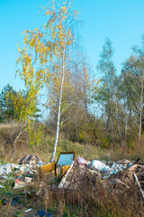 polluted area with trash and debris scattered around a field, including furniture and plastic waste.
