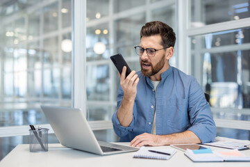 Angry and furious man shouting into phone, office worker working at workplace inside office,...