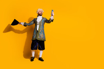Elegant nobleman in historic costume holding a smartphone on vivid yellow background with a playful mix of history and modern technology.