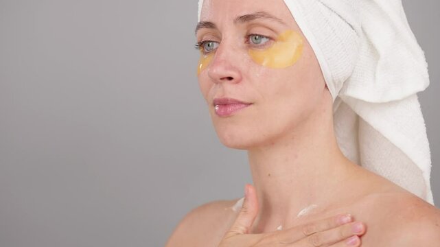Young Beautiful Caucasian woman with eye patches applying rejuvenating moisturizing cream and massage neckline skin isolated on gray studio background. Concept of Skincare Body care Beauty routine Spa