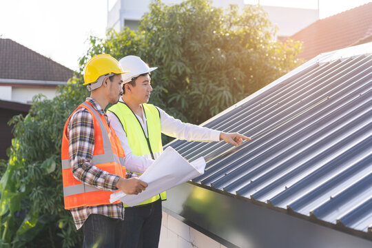 Builder team, foreman house asian young engineer, architect, contractor discussing metal sheet rooftop on blueprint follow project to build industrial plan at outdoor site. Engineering worker people.