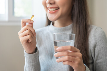 Dietary supplement, asian young woman, girl hand holding fish oil pills, drugs medical, take or eat vitamin for treatment skin, hair and nail strengthen with glass of water at home. Healthcare concept