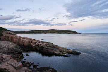 A quiet,beautiful evening on the Acadia National Park shoreline. The ocean is calm and soothing. The sky is blue and pink, and the granite rocks are a pinkish hue.