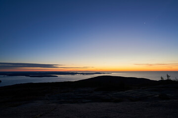An early morning view from the top of Cadillac Mountain in Acadia National Park. The sky is mostly blue, but orange and yellow can been seen at the horizon as the sun nears visibility.