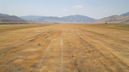 Aerial view of a vast, dry, flat field with tire tracks leading to distant mountains under a hazy sky.