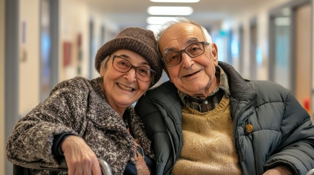 Old man pushing disabled wife on wheelchair in hospital hallway. Happy smiling senior woman in a wheelchair relaxing with her husband in care centre during a visit. Elderly man pushing his old wife.